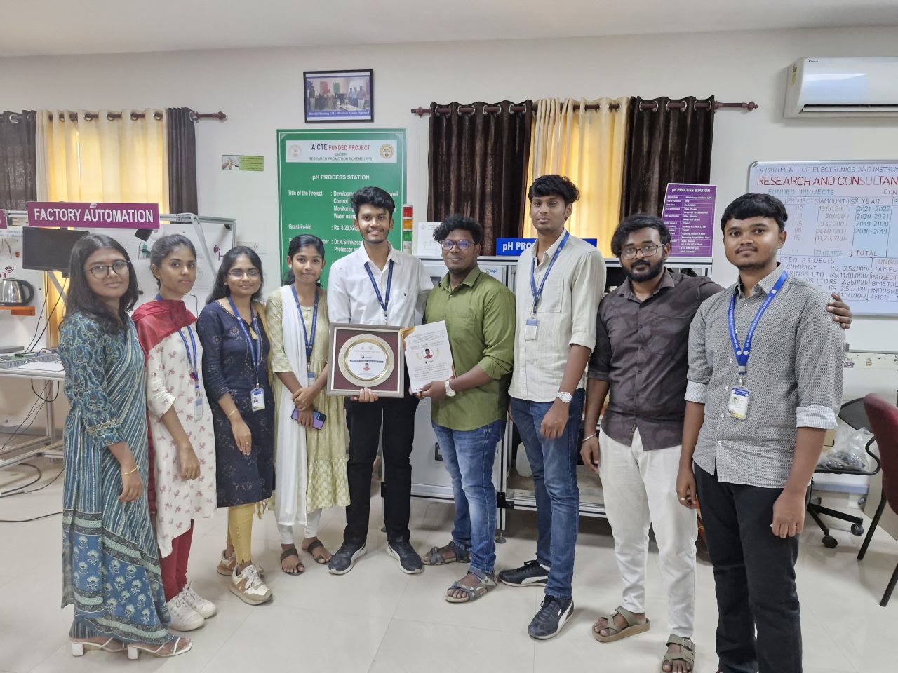 Kanish with friends in the department lab, holding the plaque and certificate